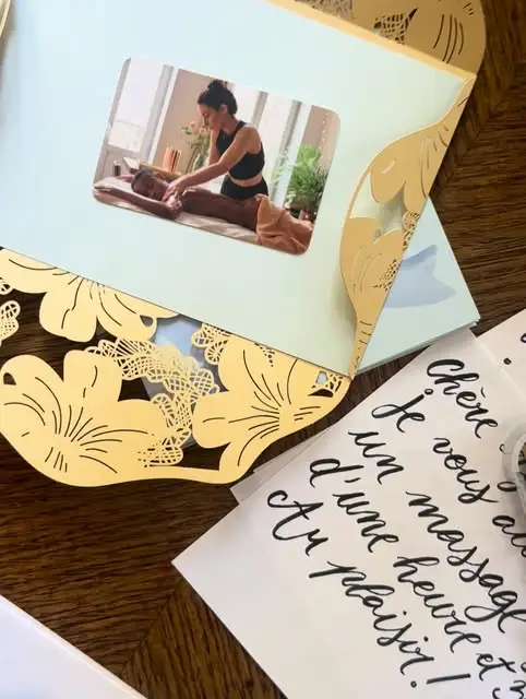 Une carte cadeau sous pochette dorée ajourée, avec une photo de Clémence en plein massage, et un texte manuscrit en calligraphie