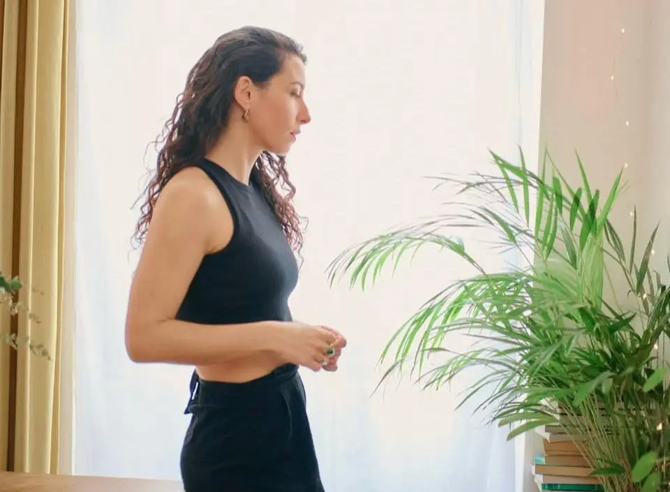 Clémence de profil devant une grande fenêtre lumineuse, à côté d’une plante