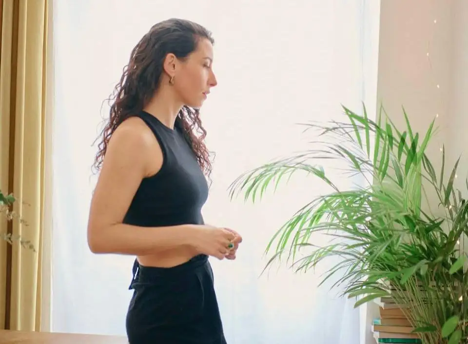 Clémence de profil devant une grande fenêtre lumineuse, à côté d’une plante